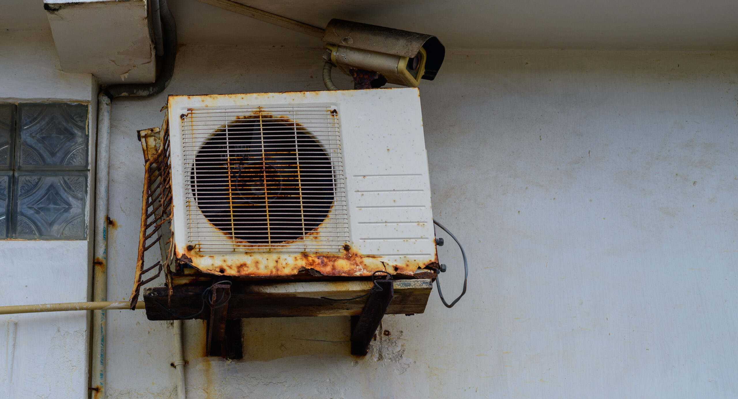 Rust air conditioner machine outdoor unit mounted onto the wall. weathered and abandoned unit close-up shot.